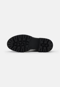 Black rubber shoe sole featuring a textured tread pattern with star-shaped lugs for traction. Flat, rounded heel design.