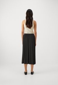 Svart plissert midi-skjørt med et tettsittende liv, parret med en lyse farget tanktop, sett bakfra. Glatt tekstur med subtil glans.