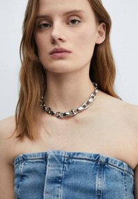 Sølvmetal kæderekæde med sammenkoblede ovale led med en poleret overflade, båret mod en bar hals uden yderligere tøjdetaljer.