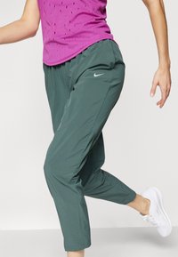 Nike sporta bikses tumši zaļā krāsā, ar elastīgu jostasvietu, sašaurinātām kājām, diskrētu sānu kabatu un mīkstu, vieglu audumu.