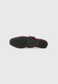 Bordowe skórzane buty o gładkiej powierzchni, okrągłym nosku i szerokiej czarnej gumowej podeszwie. Zawierają metalowy akcent w postaci sprzączki na pasku.