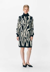 Robe tricotée avec un motif abstrait noir et crème, col haut et manches longues. Tissu texturé avec une silhouette ajustée.