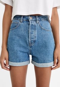 Pantalones cortos de mezclilla en azul claro con puños enrollados, que cuentan con un cierre de botón y cremallera, cinco bolsillos y una ligera textura desgastada.