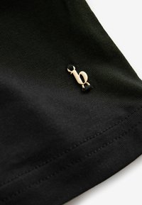 Fekete pamut póló, amelyen a szegély közelében finom arany "b" logó hímzett, texturált anyagból, tiszta, minimalista dizájnnal.