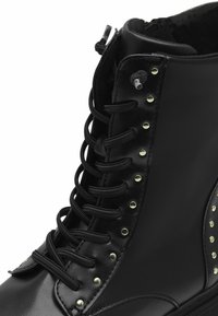 Melni lace-up potītes zābaki ar metalizētām acu caurumiem un kniedēm, gluda ādas tekstūra, mīkstināta potīte un noapaļota purngala forma.