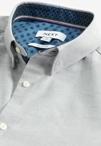 Camisa ajustada gris hecha de una tela suave, con un forro de cuello azul estampado, botones blancos y una etiqueta con la marca y el tamaño.