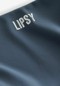 Lipsy logó tükröződő ezüst színben sötét tengerészkék anyagon, sima textúrával, enyhe fényességgel és modern dizájnnal.