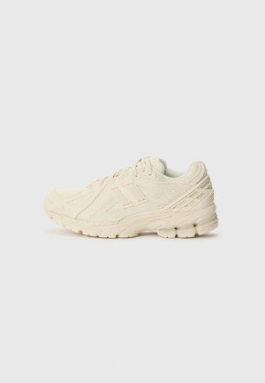 Beige athletic sneaker with mesh and leather details, lace-up closure, sturdy sole, and logo on the side, shown in left profile against plain background.