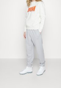 Vit sweatshirt med orange "JORDAN"-logotyp, parat med ljusgrå sweatpants med en liten Nike-logotyp. Vita sneakers med genomskinliga sulor.