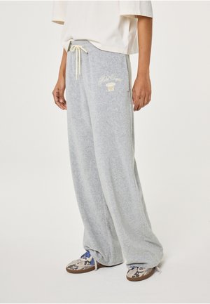 Persoon draagt lichtgrijze sweatpants met brede pijpen, trekkoord en wit grafisch ontwerp, gecombineerd met sneakers met slangenprint.