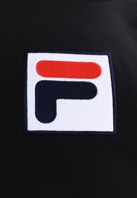 Parche cuadrado con formas abstractas en azul marino y rojo sobre un fondo blanco, cosido en tela negra.