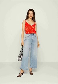 Mulher com uma blusa sem mangas vermelha e calças de cintura alta, largas, em azul claro, segurando uma bolsa com estampa de zebra e usando saltos pretos com tiras.