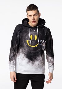 Mikina s kapucí s motivem galaxie na čern�ém pozadí, žlutý smajlík a detail astronauta. Měkká, smíchaná tkanina.
