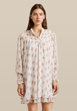 Vestido de tela blanca ligera y transparente con un estampado floral, presenta un diseño plisado, cuello, mangas largas y detalles de dobladillo con volantes.
