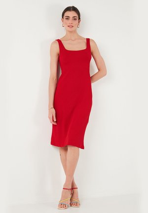 Red ribbed midi dress with a square neckline, fitted silhouette, and straight hem. Worn with multi-colored strappy sandals.