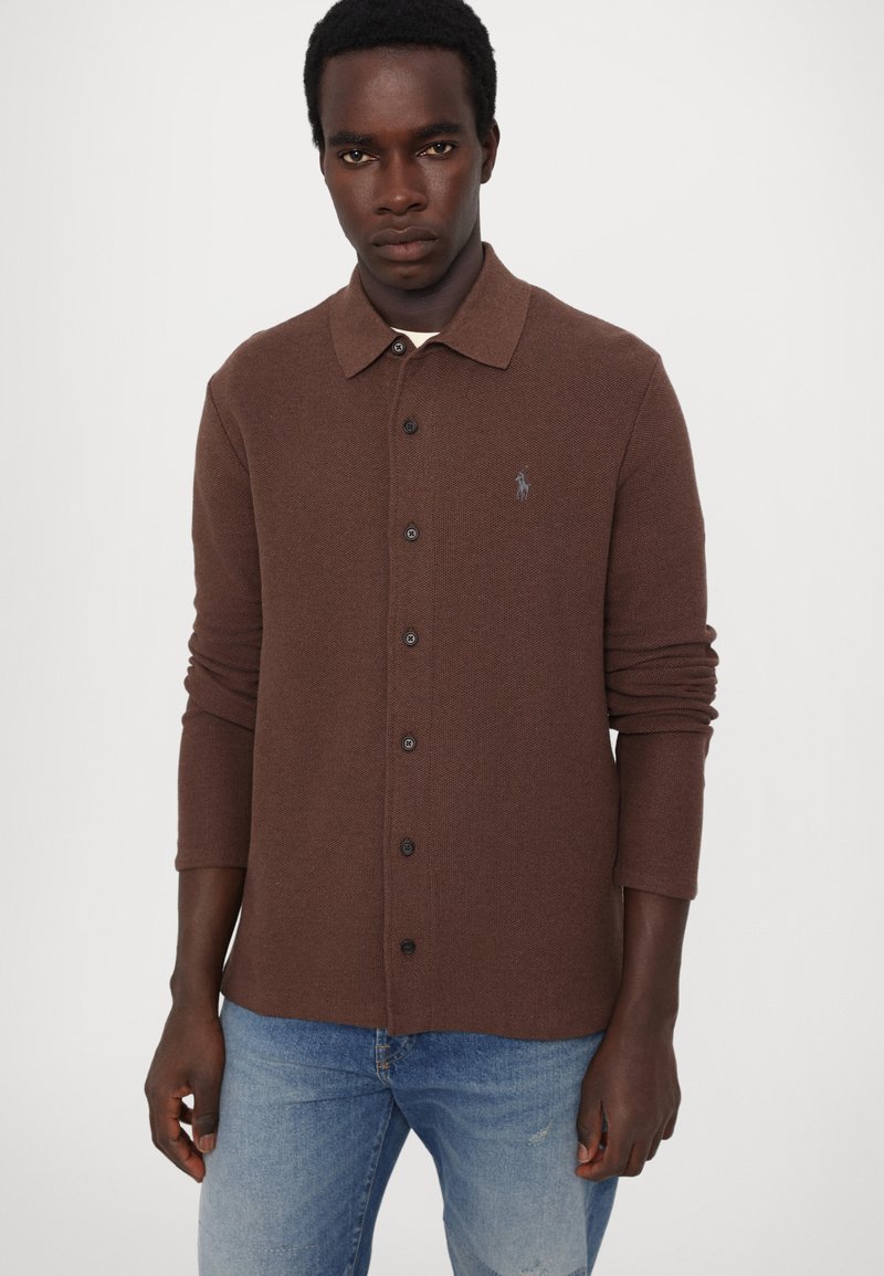 Braunes Hemd mit Knopfleiste aus strukturiertem Stoff und langen Ärmeln. Verfügt über einen Kragen und ein kleines Logo auf der Brust.