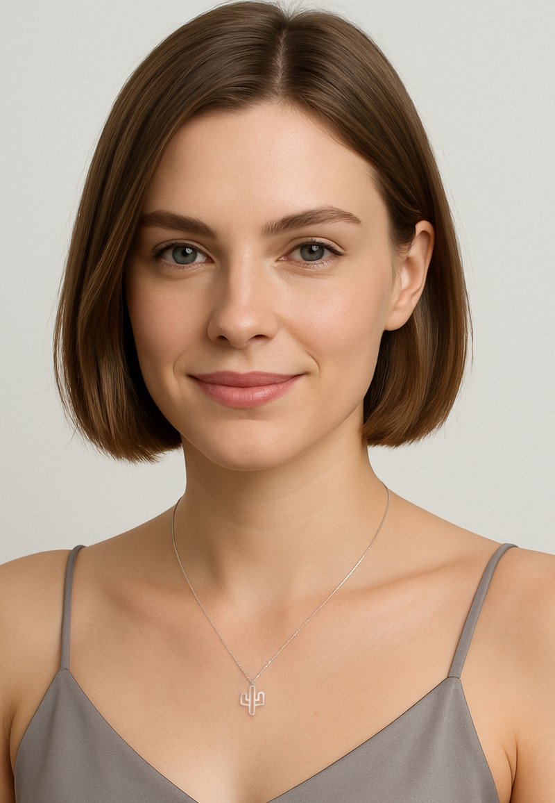 Collana a pendente a forma di cactus in argento che pende su una catena sottile, indossata da una persona con un top grigio chiaro. Finitura metallica liscia, design semplice.