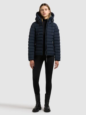 Marineblaue gesteppte Jacke mit Kapuze, ausgestattet mit einem Reißverschluss und Kordelzügen. Trägt man über einem schwarzen Rollkragenpullover und Leggings, kombiniert mit schwarzen Stiefeln.