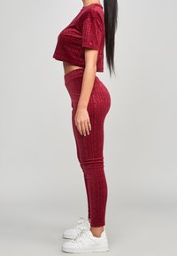 Conjunto de top corto y leggings a juego en burdeos, hecho de una tela texturizada con un sutil patrón de logotipos, combinado con zapatillas blancas.