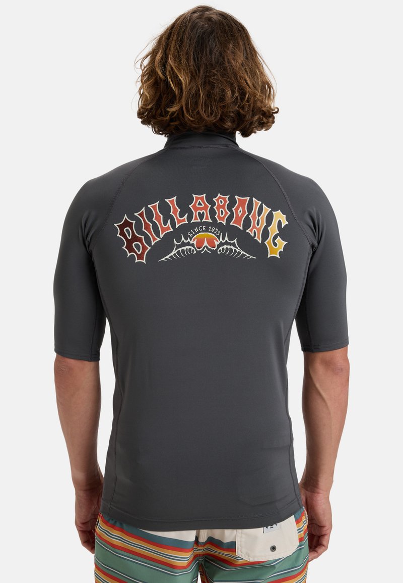 Mörkgrå rash guard med korta ärmar och en färgglad "Billabong"-logotyp med stiliserad text och mönster över ryggen.