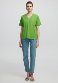 T-shirt verde a collo a V in cotone, maniche corte, vestibilità comoda, abbinata a jeans in denim azzurri chiari e sandali piatti.