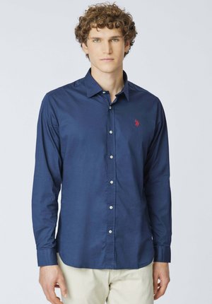 Camicia blu navy a maniche lunghe con bottoni in tessuto di cotone, caratterizzata da un colletto classico, bottoni bianchi e un piccolo logo rosso ricamato sul petto.
