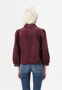 Burgundi värvi sametjakk, millel on krae, puhv- varrukad ja nööbid mansettides, koos siniste teksapükstega.