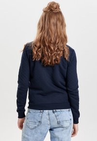 Marinblå quiltad sweatshirt med långa ärmar och ribbad mudd, i kombination med ljusblå jeans med bakfickor och synliga söm detaljer.