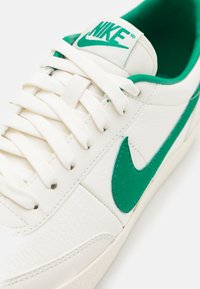 Valge nahast spordijalats roheliste aktsentidega, millel on silmapaistev roheline Nike silt, valged paelad ja tekstureeritud viimistlus.