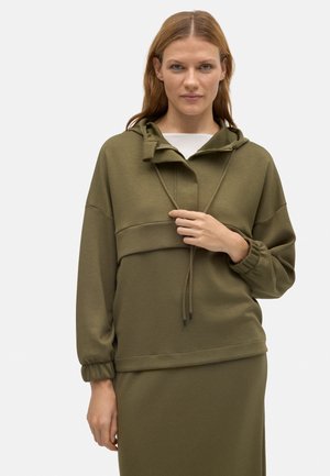 Sudadera con capucha de color verde oliva con cordones, mangas largas y puños fruncidos. Textura suave y corte relajado, llevada sobre una camiseta blanca.