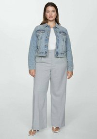 Denimjakke i lyseblå, tætsiddende i taljen, to brystlommer; parret med højtaljede, grå stribede vide bukser og hvide sandaler.