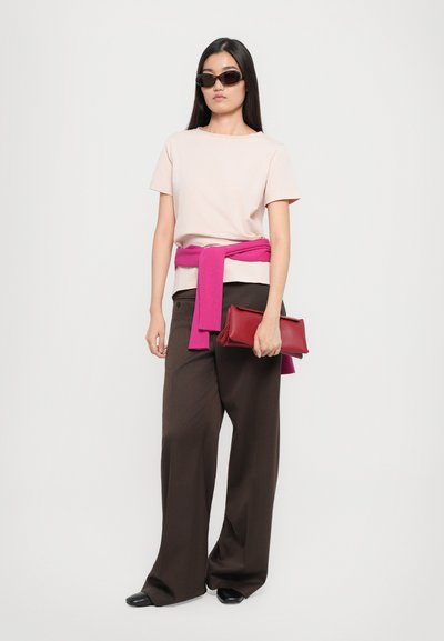 Light pink t-shirt, pink knit sweater tied at the waist, brown wide-leg trousers, black shoes, and a red clutch bag. Brown sunglasses.