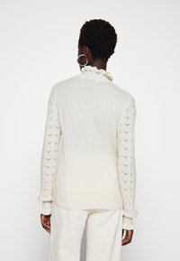 Maglione di colore crema chiaro con colletto arricciato, maniche testurizzate con un motivo a foglia e polsini a coste. Tessuto in maglia morbido con una vestibilità comoda.