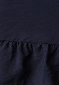 Tissu bleu marine foncé avec couture visible et détail de volants froncés créant texture et plis.