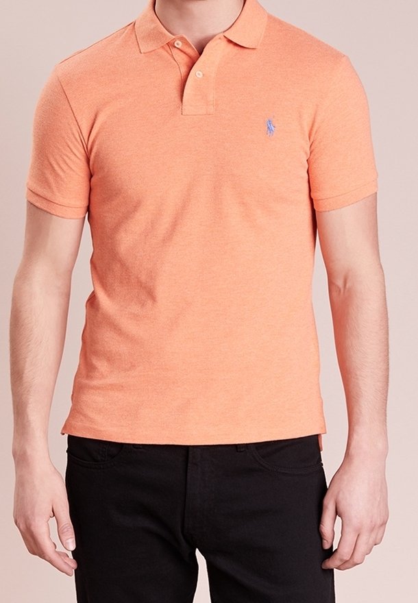 Homme portant un polo orange près du corps à manches courtes avec un petit logo bleu brodé sur la poitrine et un pantalon noir.
