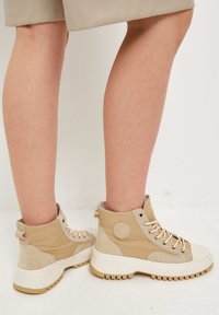 Beige vysoké tenisky vyrobené z semišového a plátěného materiálu. Mají kulatý akcent, kontrastní tkaničky a silnou bílou podrážku.