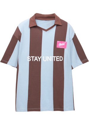 Brązowa i jasnoniebieska w paski, krótka koszulka polo z dekoltem w kształcie litery V; posiada różową metkę z napisem "STAY UNITED" w kolorze białym.