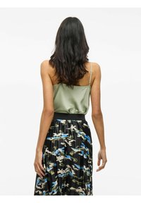 Olivgrüne Satin-Camisole mit dünnen Trägern, kombiniert mit einem gefalteten schwarzen Rock, der blaue, grüne und beige abstrakte Muster aufweist.