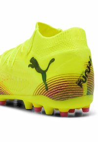 Svijetložuti nogometni kopački s teksturiranim gornjim dijelom, zelenim Puma logotipom i šarenim gradijentnim dizajnom duž potplata s ružičastim akcentima.