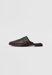 Black slip-on mule made of textured material with a reptile pattern, featuring a low, flat heel and a rounded, open toe design.