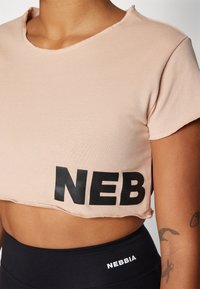 Lys rosa avkortet t-skjorte med råkant, med fet svart "NEB" foran. Slett tekstur, rund halslinning og korte ermer.