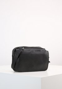 Svart läder crossbody-väska med texturerad yta, rektangulär form, dragkedjestängning och avtagbar rem.