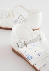 Weiße synthetische Sandalen mit einem gewobenen Riemendesign und einer silbernen Schnalle. Der floral gemusterte Innensohle zeigt hellblaue Blumen auf einem weißen Hintergrund.