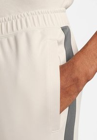 Los pantalones jogger color crema cuentan con una cinturilla elástica, un bolsillo lateral y una franja gris en contraste a lo largo de la costura lateral. Textura de tela suave.