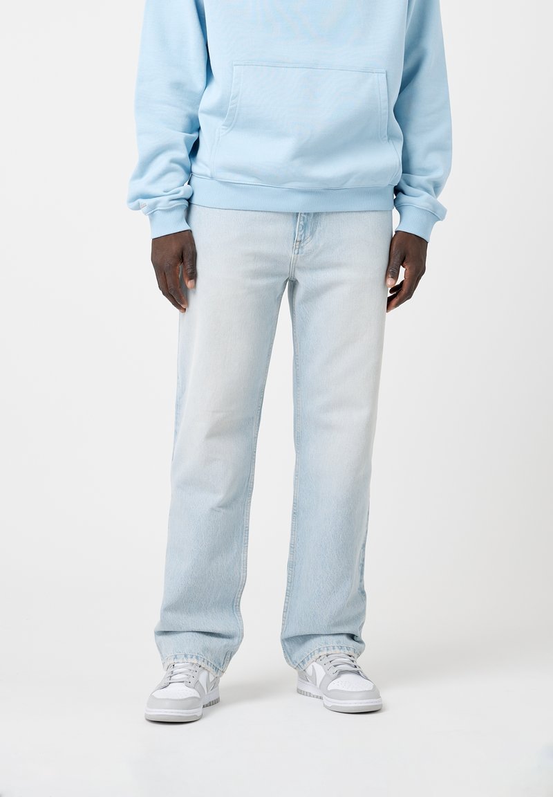 Jasnoniebieska bluza z kapturem z przednią kieszenią, w połączeniu z jasnoniebieskimi dżinsami i białymi sneakersami. Luźny krój, prosty design i miękka tekstura.