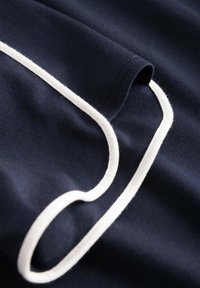 Marineblauwe stof met witte biesafwerking, gladde textuur en afgeronde randen. Inzoomen toont de stiksels en contouren.