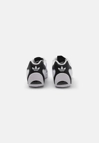 Λευκά και μαύρα αθλητικά παπούτσια με μαλακή υφή, διαθέτοντας λογότυπο στη φτέρνα, στρογγυλεμένο σχήμα και καουτσούκ σόλα.