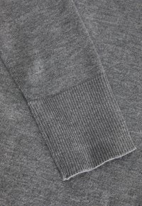 Grå tröjsleeve med ribbad manschett och mjukt, texturerat tyg med en lätt marbledesign och en ren avslutning.