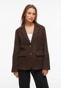 Blazer de camurça castanho com dois bolsos frontais, fecho de botão único, lapelas dentadas e mangas longas. Textura suave, ajuste sob medida.
