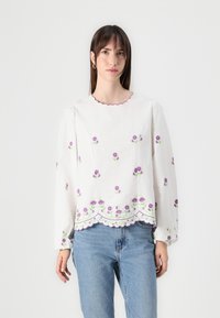 Blusa bianca con ricami floreali viola, colletto scallop e maniche lunghe a sbuffo. Finitura con un orlo in pizzo decorativo. Tessuto leggero.